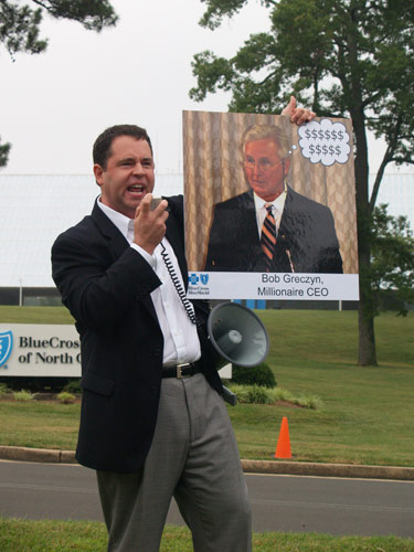 SEANC Executive Director Dana Cope holds up a photo of BCBSNC CEO 
Bob Greczyn as he exhorts health care reform advocates to band together. Photo by Taylor Sisk.